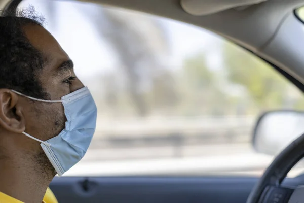 An Arabic man in the United Arab Emirates driving between Al Ain and Abu Dhabi wearing a protective face mask