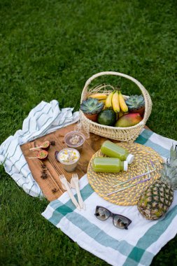 Vejetaryen pikniği. Tahta bir arka planda tropikal meyve mangosu, ananas, muz ve maracuu tezgahından tatlılar. Yanında iki yeşil meyve suyu şişesi ve bir sepet tropikal meyve var. Diyet yemek.