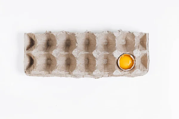 Paper box for chicken eggs on a white background with one egg broken egg. The yolk is in the shell. The ingredients for the omelet. Farm eggs. Eggs are light in color. The lack of food.