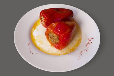 Lezzetli pişirilmiş kırmızı dolma biber, et ve pirinçle doldurulmuş. Beyaz tabakta servis edilen lezzetli sos ve gri arka planda izole edilmiş paprika baharatı. 