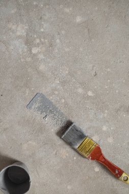 Beton zeminde boyanmış ahşap bir boya fırçası var. Yakınlarda camdaki gri boya..
