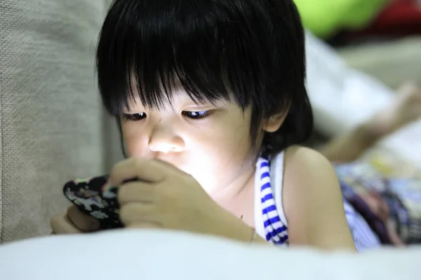眠そうな子供産む床とプレイのスマート フォンでアジアのかわいい子供はスマート フォンでゲームをプレイ — ストック写真