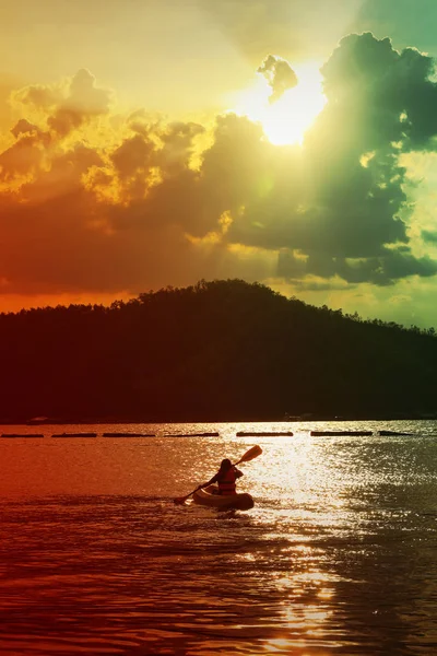 女の子は湖でカヤックをしていて、山の後ろの夕日 — ストック写真