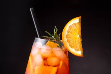 Portakal ve biberiye dilimleriyle süslenmiş bir şarap kadehinde servis edilen Aperol spreyine yakın bir yerde.