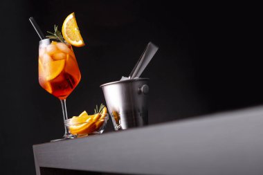 Aperol spritz cocktail served in a wine glass with lots of ice, decorated with slice of orange and rosemary branch, placed on a bar counter clipart