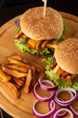 Tahta tepside soğan ve patates kızartması ile servis edilen lezzetli taze burgerlerin yüksek açılı görüntüsü.