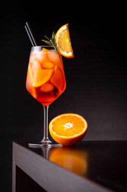 Glass of Aperol spritz cocktail served in a wineglass, decorated with slices of orange and rosemary branch, placed on a bar counter clipart