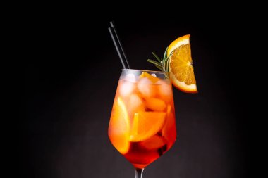 Portakal ve biberiye dilimleriyle süslenmiş bir şarap kadehinde servis edilen Aperol spreyinin detayları.