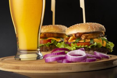 Bir bardak soğuk bira ve bar tezgahındaki ahşap tepsiye yerleştirilmiş hamburgerlerin ayrıntıları; fast food ve soğuk bira.