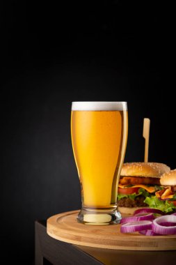 Bir bardak soğuk soluk bira ve bar tezgahındaki ahşap tepsiye birkaç hamburger; fast food ve bira.