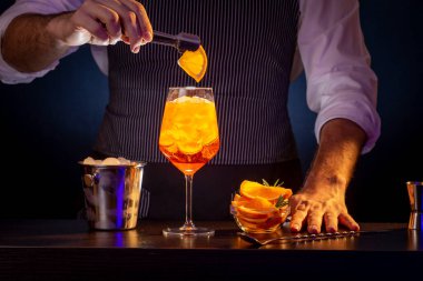 Barmen Aperol sprey kokteyli dekore ediyor, buzla dolu bir şarap kadehine bir dilim portakal ekliyor.