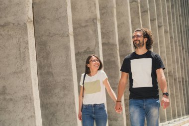 Güzel, genç aşık bir çift güneşli bir yaz gününde dışarıda eğleniyor, sokakta yürüyor, gülümsüyor ve el ele tutuşuyorlar.