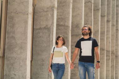 Güzel bir genç çift şehir turunda eğleniyor, tatildeyken seyahat ediyor, sokakta yürüyor, gülümsüyor ve el ele tutuşuyor.