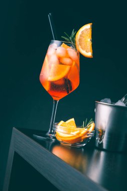 Aperol spritz cocktail served in a wine glass, decorated with slice of orange and rosemary branch, placed on a bar counter clipart