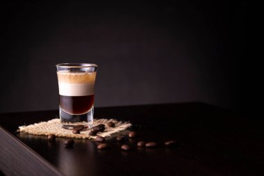 B-52 katmanlı bir kokteyl bardağının üzerine yerleştirilmiş taze kavrulmuş kahve çekirdekleri ve fotokopi alanı.