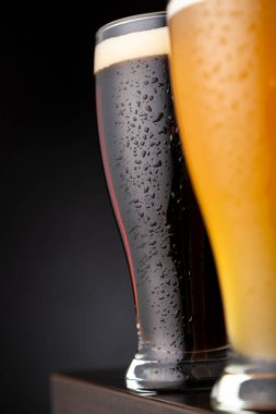 İki bardak soğuk filtresiz buğday birası ve bir bar tezgahına koyulmuş koyu bira.