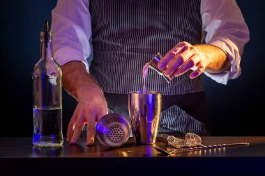 Barmen kokteyl hazırlıyor, malzemeleri ölçü kabından karıştırıcıya döküyor.