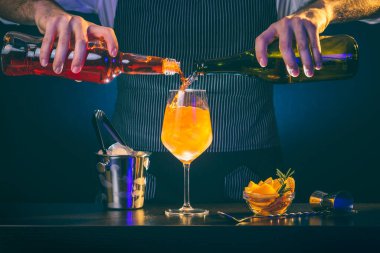 Barmen Aperol spritz kokteyli hazırlıyor, Prosecco ve Aperol 'u buzla dolu bir şarap bardağına döküyor.