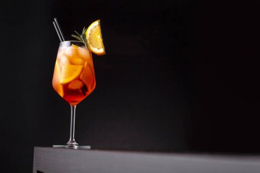 Glass of orange cocktail served in a wine glass, decorated with slices of orange and rosemary branch, placed on a bar counter clipart