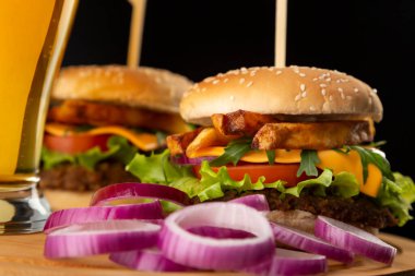 Bir bardak soğuk bira ve bar tezgahındaki ahşap tepsiye yerleştirilmiş hamburgerlerin ayrıntıları; fast food ve soğuk bira.