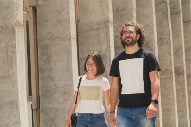 Güzel, genç aşık bir çift el ele tutuşuyor ve şehir caddesinde yürüyor güneşli bir yaz gününün tadını çıkarıyorlar.