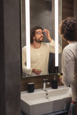 Banyoda aynanın önünde pijama giyen yakışıklı genç bir adam. Geceleri uyumadan önce kişisel hijyen rutini uyguluyor.