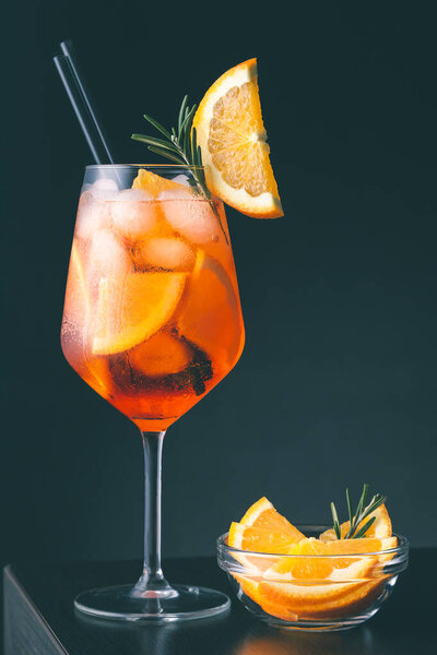 Коктейль Aperol spritz подается в винном бокале, украшенном ломтиком апельсина и розмарином, помещенным на барной стойке