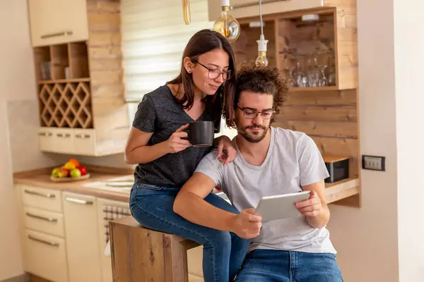 年轻夫妇喜欢喝咖啡 喜欢在厨房里用平板电脑 喜欢早上在家里放松 — 图库照片
