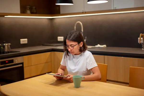 Νεαρή Γυναίκα Φορώντας Πιτζάμες Κάθεται Στο Τραπέζι Της Κουζίνας Διαβάζοντας — Φωτογραφία Αρχείου
