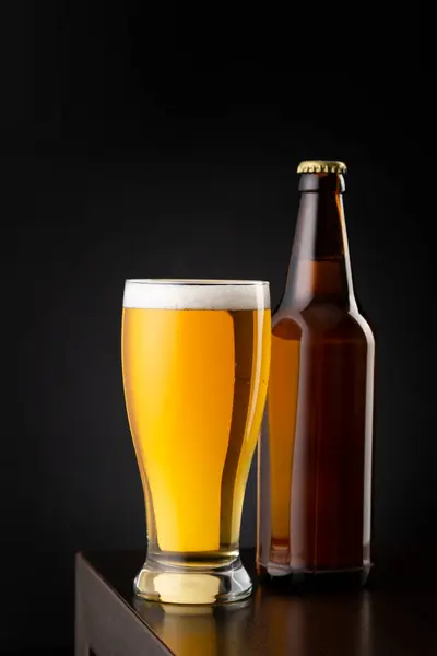 一杯冷的淡啤酒和一个啤酒瓶放在吧台上 — 图库照片