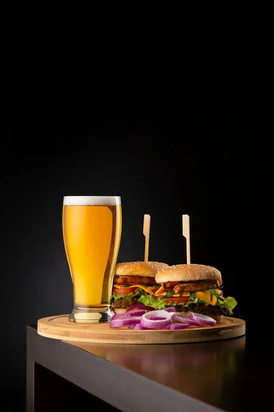 冷的淡啤酒和一些汉堡包放在酒吧柜台的木制托盘上 上面有抄袭空间 快餐和啤酒 — 图库照片