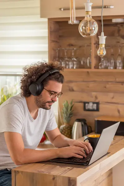 Hombre Sentado Mostrador Cocina Con Auriculares Trabajando Ordenador Portátil Forma —  Fotos de Stock