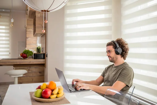 Jovem Sentado Mesa Cozinha Vestindo Fone Ouvido Trabalhando Computador Portátil — Fotografia de Stock