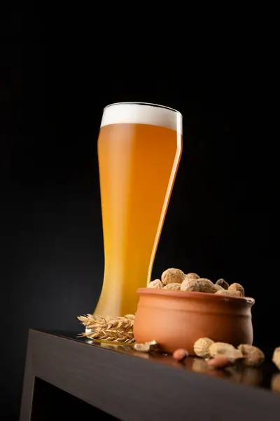 Glass of cold unfiltered wheat beer and a bowl of unshelled peanuts on a bar counter