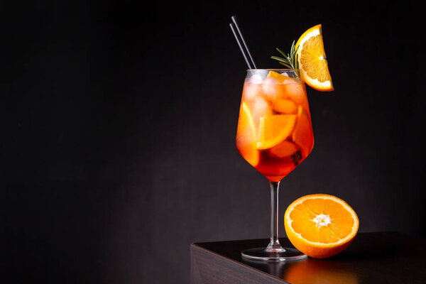 Glass of Aperol spritz cocktail served in a wine glass, decorated with slices of orange and rosemary branch, placed on a bar counter