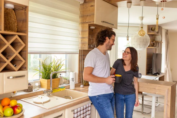 Young couple in love standing in the kitchen, drinking their morning coffee and hugging while relaxing at home