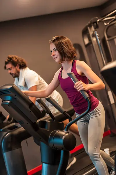 在健身房用滑雪机进行心血管训练的年轻夫妇 在健身中心做有氧运动的人 — 图库照片