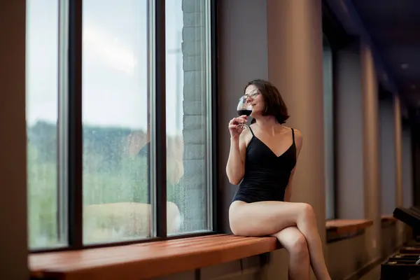 Piękna Młoda Kobieta Stroju Kąpielowym Siedząca Przy Oknie Pijąca Wino — Zdjęcie stockowe