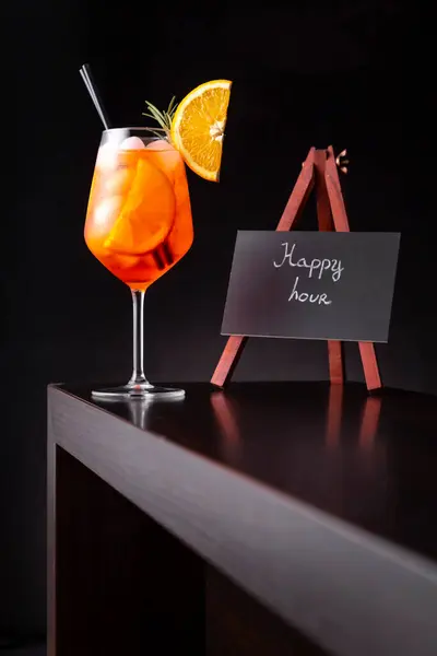 Low angle view of orange cocktail served in a wineglass, decorated with slice of orange and rosemary branch, placed on a bar counter
