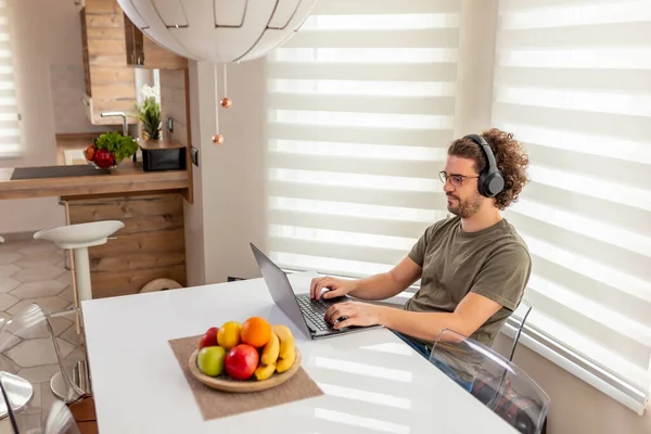 Jovem Sentado Mesa Cozinha Vestindo Fone Ouvido Trabalhando Computador Portátil — Fotografia de Stock