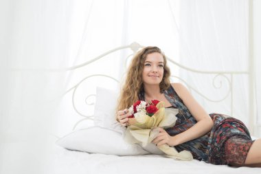 Yatakta çiçek buketiyle yatan güzel bir genç kadının portresi.