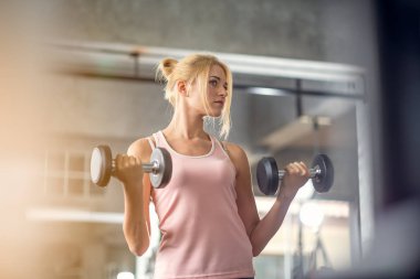 Güçlü kadın dambıllarla çalışıyor, spor salonunda egzersiz yapıyor.