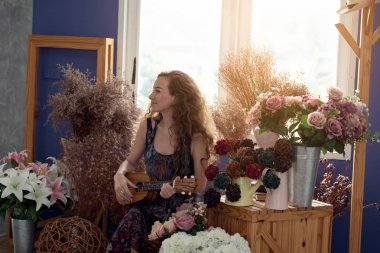 Genç gülümseyen kadın müzik zamanında Ukulele çalarak eğleniyor ve dinleniyor.