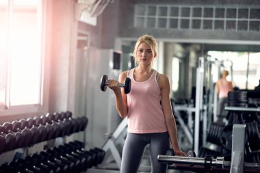 Güçlü kadın spor salonunda dumbbells ile yapıyor