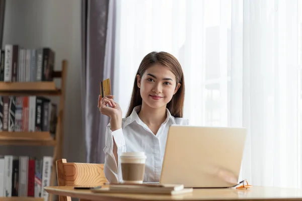 Молодая азиатка держит кредитку и думает об онлайн-шо — стоковое фото