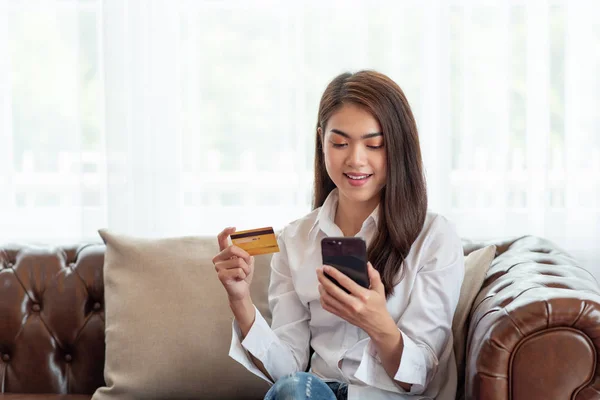 Mujer asiática joven sosteniendo la tarjeta de crédito y el uso de teléfono móvil, En —  Fotos de Stock