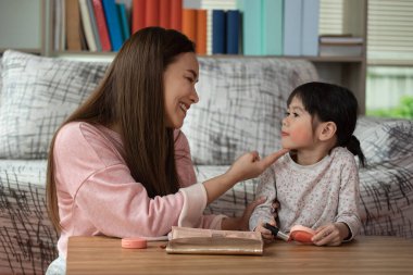 Mutlu çocuk, küçük Asyalı kız annesiyle makyaj yapıyor, sevgi dolu aile kavramı.