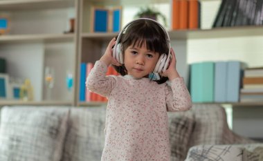 Mutlu Asyalı çocuk kulaklıkla müzik dinlerken ve bir odada dans ederken eğleniyor. Aktif eğlence ve yaşam tarzı kavramı.