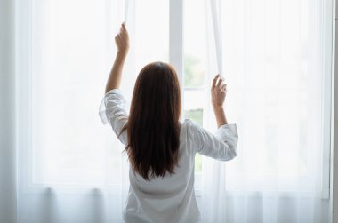 Genç Asyalı kadının portresi sabah uyandıktan sonra perdeyi açıyor.