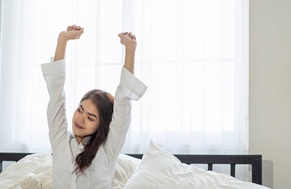Portrait of young Asian woman stretching in bed after wake up in the morning